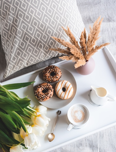 Café da manhã na cama com uma xícara com cappuccino, rosquinhas e tulipas brancas