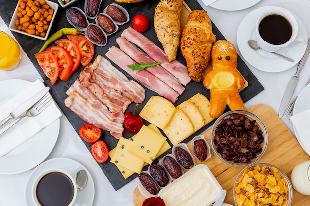 Café da manhã na mesa. pão de croissant, cereal de croissant, bacon, presunto, queijo, alface, feijão, flocos de milho, frutas, café, chá e suco de laranja é o café da manhã. , almoço ou jantar todos os dias