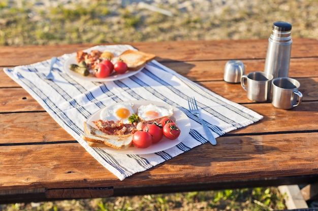 Café da manhã na natureza ovos fritos com torradas de bacon frito e café quente em uma garrafa térmica