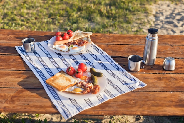 Café da manhã na natureza ovos fritos com torradas de bacon frito e café quente em uma garrafa térmica