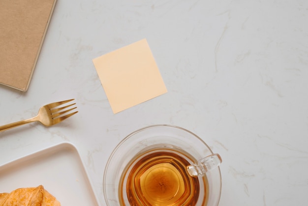 Café da manhã na sala de estar com croissant francês, xícara de chá, caneta e caderno na mesa de pedra