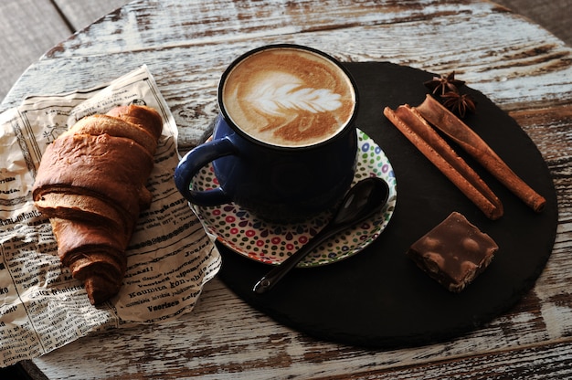 Café da manhã no café cappuccino em uma caneca, croissant, canela