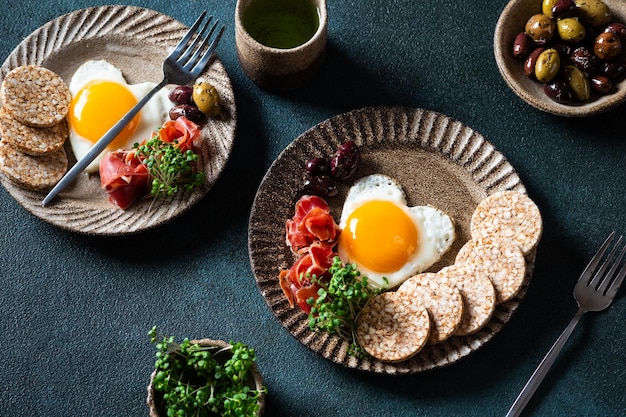 Café da manhã no dia dos namorados ovos fritos em forma de coração e azeitonas Café da manhã saudável Bolos de arroz com ovos e presunto Café da manhã romântico Vista superior