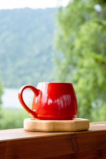 Café da manhã no jardim Caneca vermelha na placa de madeira contra a natureza turva