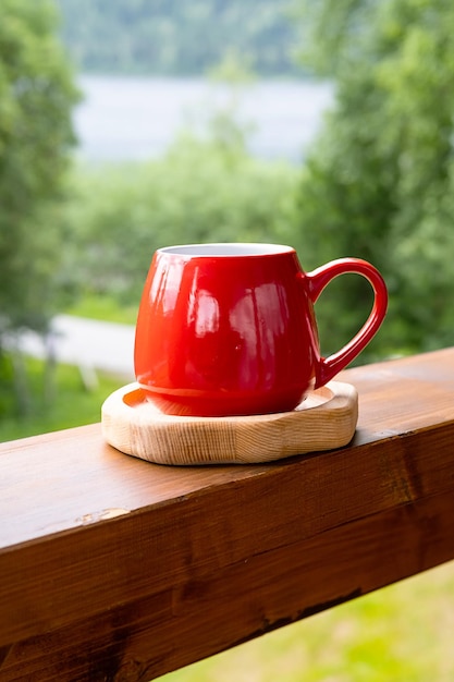 Café da manhã no jardim Caneca vermelha na placa de madeira contra a natureza turva