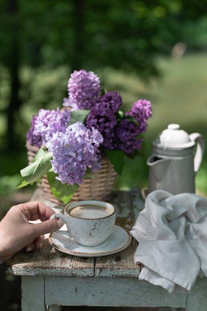 Café da manhã no jardim: doces, xícara de café, cafeteira, flores lilás em uma cesta.