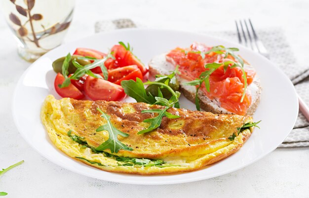 Café da manhã. Omelete com queijo, rúcula verde e sanduíche com salmão na chapa branca. Frittata - omelete italiana.