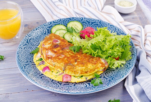 Café da manhã. Omelete com rabanete, cebola vermelha e salada fresca na placa azul. Frittata - omelete italiana.