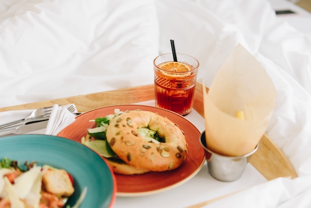 Café da manhã ou almoço na cama de uma salada de panzanella com croutons e um pão com alface fresca, duas bebidas e batatas fritas