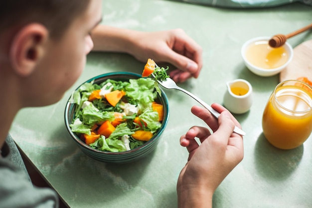 Foto café da manhã ou almoço vegano menino adolescente tomando café da manhã salada de vitaminas de inverno na mesa branca com um verde