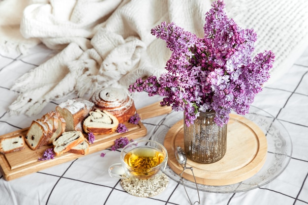 Café da manhã ou brunch na cama com bolos e chá. Buquê lilás em um vaso. Romance e férias.