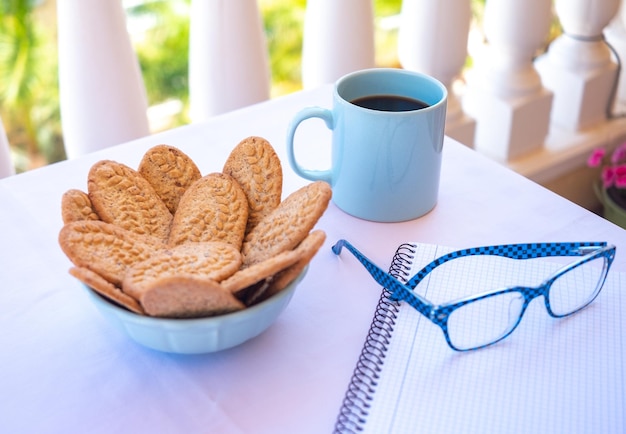 Café da manhã ou momento de pausa ao ar livre na varanda com xícara de café e biscoitos integrais Caderno para escrita e óculos