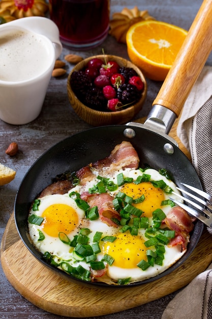 Café da manhã ovos mexidos com bacon, café, frutas, biscoitos, nozes e suco na superfície da mesa escura