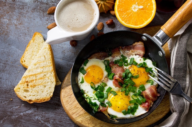 Café da manhã ovos mexidos com bacon, café, frutas, biscoitos, nozes e suco na superfície da mesa escura