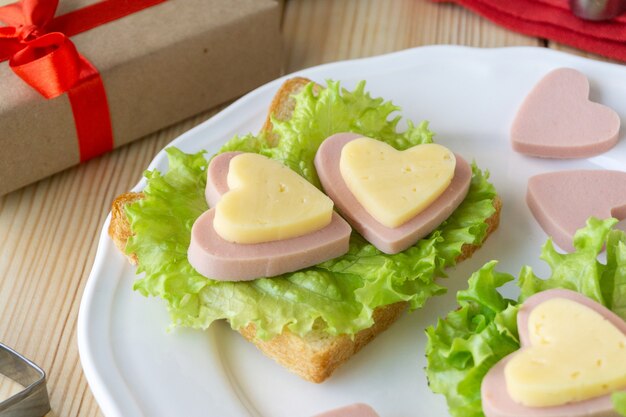 Café da manhã para o dia dos namorados. Sanduíche com salsicha, queijo e alface na chapa branca.