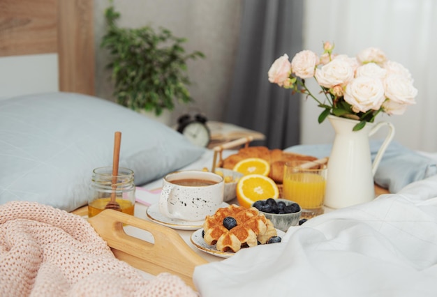 Café da manhã romântico com café, waffles, suco de laranja e flores rosas.