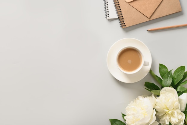 Café da manhã romântico de verão com xícara de café e flores de peônias brancas na mesa de escritório cinza