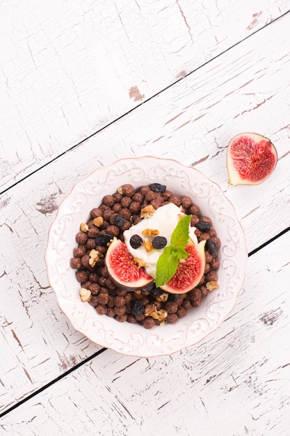 Café da manhã saudável: bacia de bolas do chocolate com iogurte e figos frescos na tabela de madeira branca.