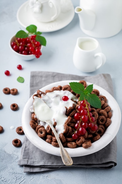 Café da manhã saudável com anéis de milho de chocolate, groselha, iogurte e chá em um fundo cinza de concreto