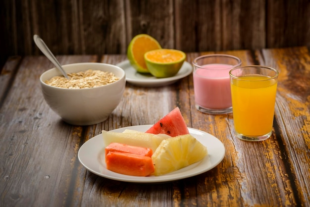 Café da manhã saudável com frutas, aveia e iogurte na mesa de madeira.