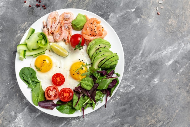 Café da manhã saudável com salmão, camarão cozido, camarão, ovos fritos, salada fresca, tomate, pepino e abacate. dieta ceto. lugar da receita do menu para texto, vista superior.