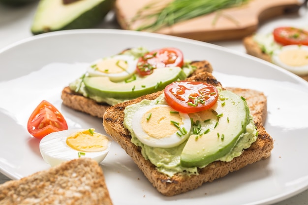 Café da manhã saudável de torradas com abacate, molho de ovo de guacamole, tomate e cebolinha.