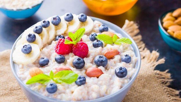 Foto café da manhã saudável porridge de aveia com bagas frutas e mel em fundo escuro