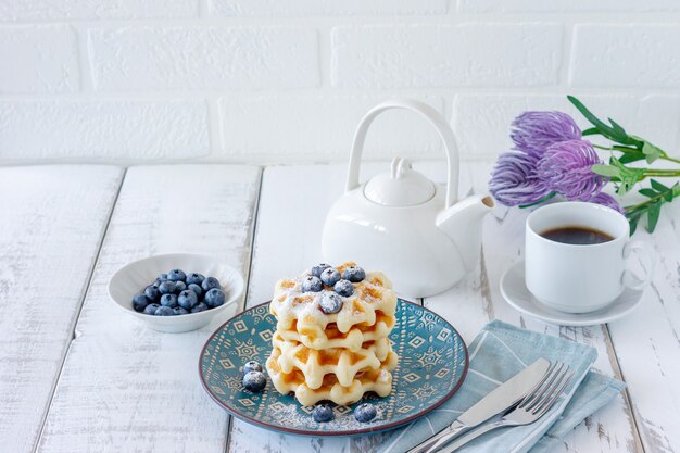 Café da manhã saudável. Waffles belgas com mirtilos, açúcar em pó e mesa de chá na madeira.