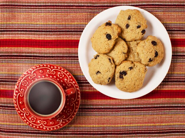 Café da manhã servido, café com biscoitos. Tom quente avermelhado. fotografia de cima para baixo. copo vermelho decorado