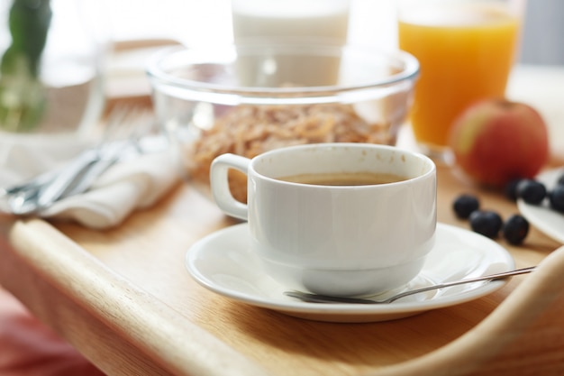 Café da manhã servido na cama na bandeja de madeira com café e croissants