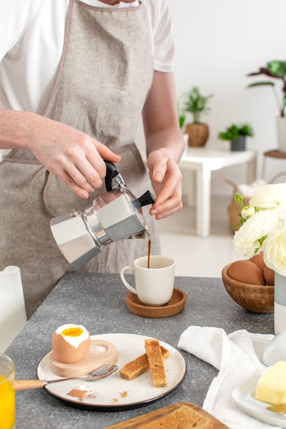 Café da manhã servido, pão torrado, ovo cozido, mãos femininas derramando café de moka