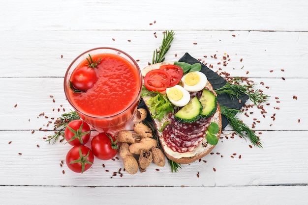 Café da manhã Suco de tomate e hambúrguer com salame e legumes Em um fundo de madeira Vista superior Copiar espaço