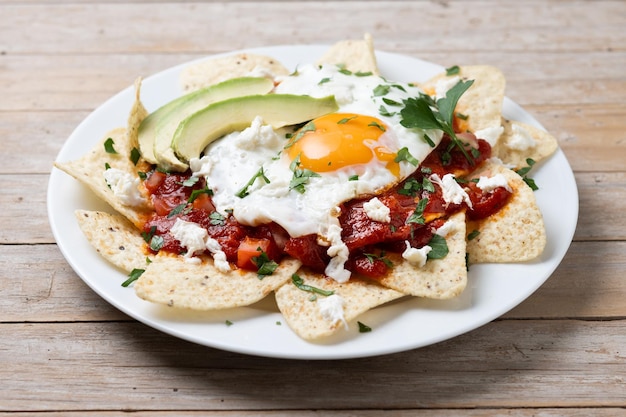 Foto café da manhã tradicional mexicano chilaquiles vermelhos com ovo em mesa de madeira