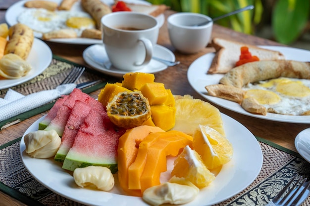 Café da manhã tropical com café de frutas e ovos mexidos e panqueca de banana para dois na praia perto do mar
