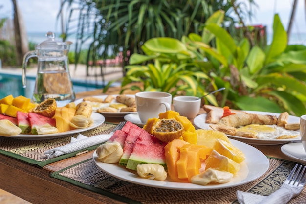 Café da manhã tropical com frutas, café, ovos mexidos e panqueca de banana para dois na praia perto do mar no restaurante do hotel, ilha de Zanzibar, Tanzânia, África, close-up