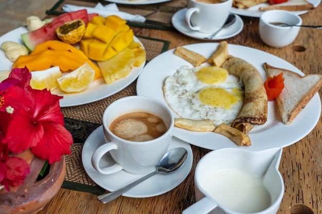 Foto café da manhã tropical de frutas, café e ovos mexidos e panqueca de banana