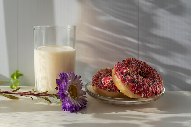 Café da manhã, um copo de leite e donuts frescos em um raio de sol.