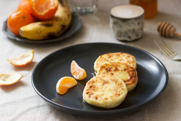 Café da manhã vegetariano de panquecas de quark com mel, frutas e café com leite. Estilo rústico.