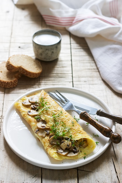 Café da manhã vegetariano, omelete com cogumelos e agrião, servido com pão de centeio e café com leite. estilo rústico.