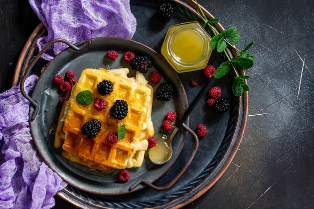 Café da manhã waffles belgas caseiros com frutas vermelhas e mel na mesa escura vista de cima plana lay