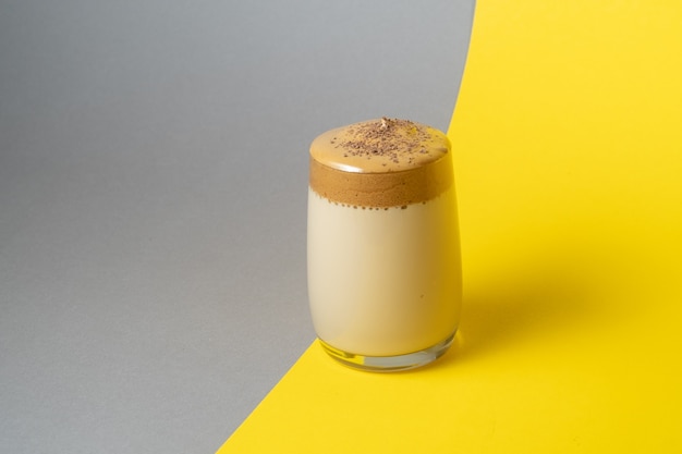 Café Dalgona com espuma exuberante em um copo sobre fundo amarelo e cinza. Bebida coreana da moda.