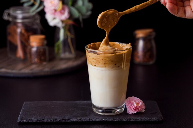 Café dalgona en vaso de vidrio Café instantáneo esponjoso con leche fría Flor de sakura decorada con coronavirus de cuarentena