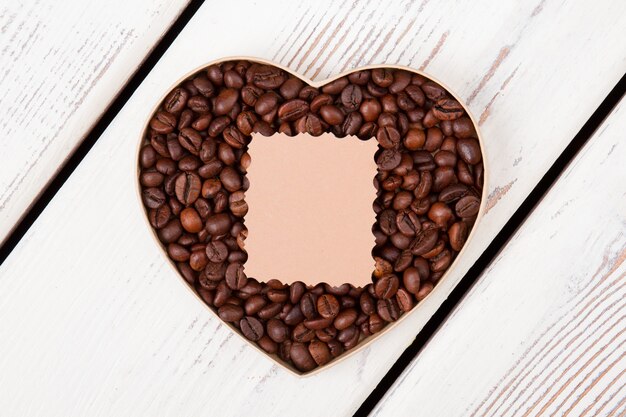 Café para el día de San Valentín. Granos de café dispuestos en forma de corazón y papel en blanco para copyspace.