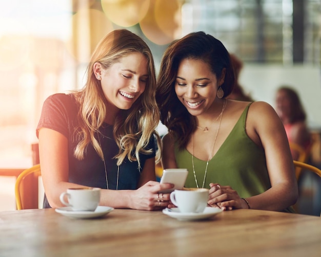 Café e amigos é melhor quando você os junta Foto recortada de amigas compartilhando algo no celular enquanto estão sentadas em um café