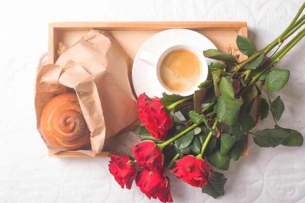 Café e bolos em uma bandeja de madeira. Com um buquê de flores na cama.