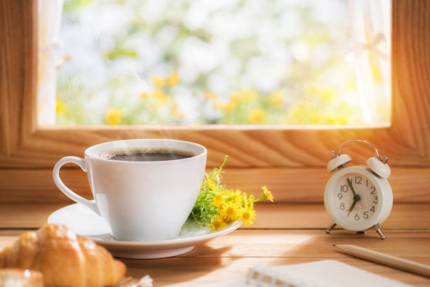 Café e flores para o café da manhã colocados perto da janela com o sol da manhã