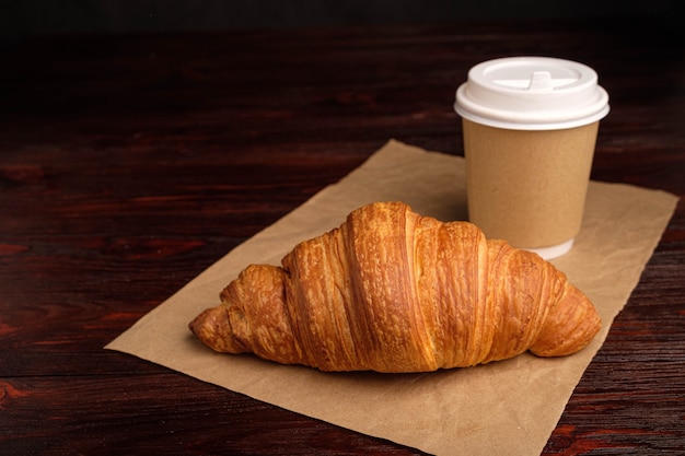 Café em copo de papel e croissant na mesa de madeira