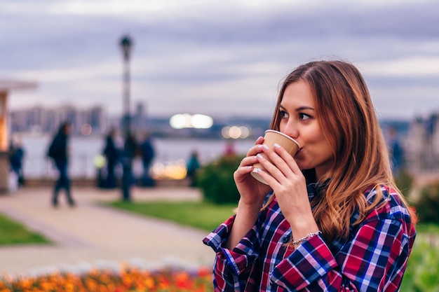 Café em movimento. Mulher jovem e bonita tomando café no parque