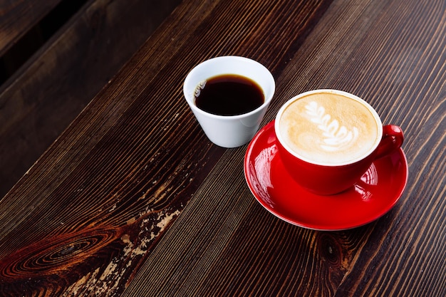 Café em um copo vermelho com leite e café com leite e café em um copo branco sobre uma mesa
