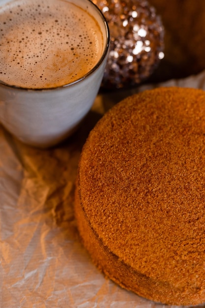 Café em uma caneca de designer e bolo de mel caseiro em uma mesa de madeira em uma atmosfera de ano novo